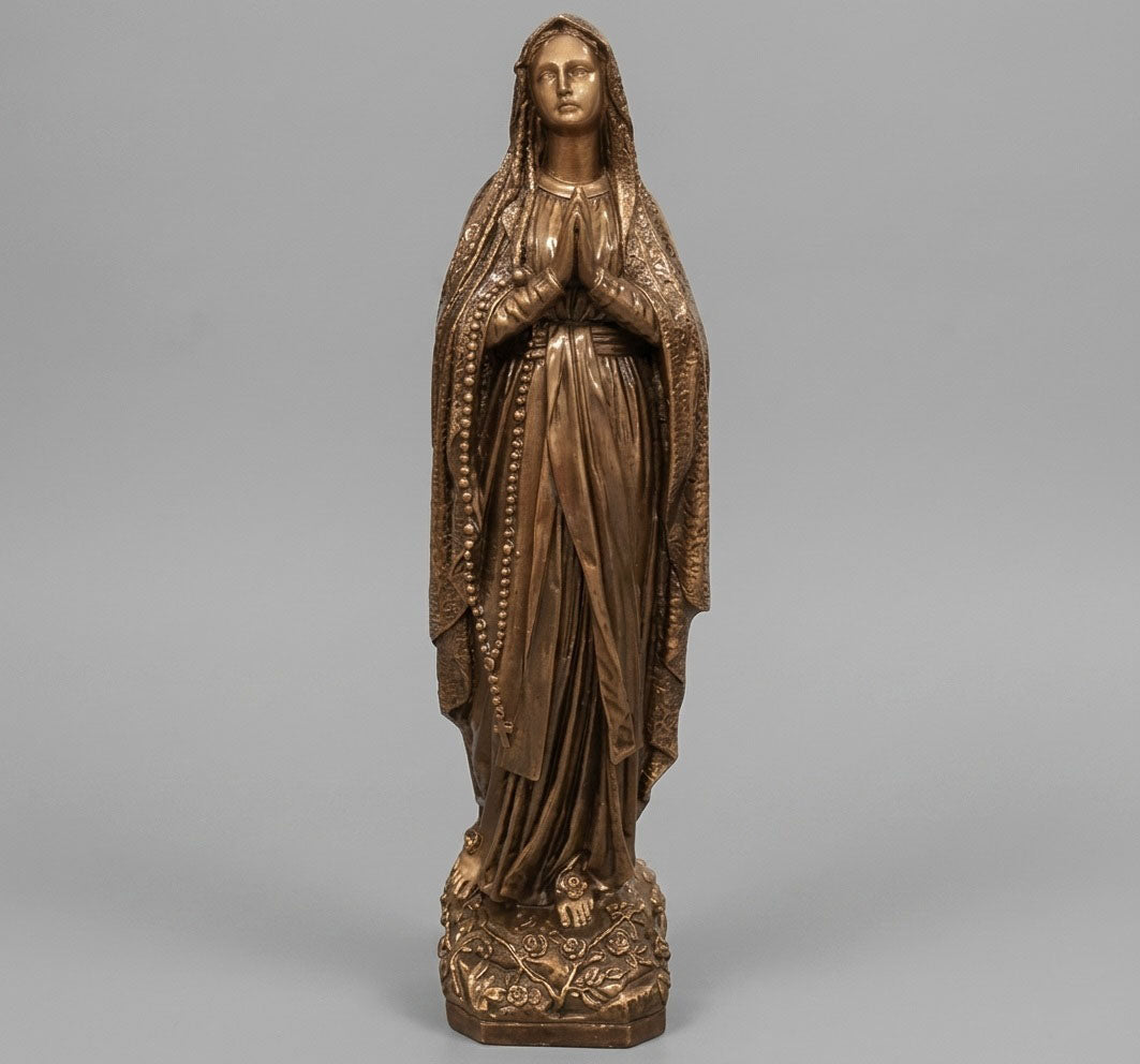 Escultura de la Virgen de Lourdes (62 cm) en mármol sintético con elegante acabado bronce. Referencia MR 7070 B, diseñada con fijación a suelo para máxima estabilidad en cementerios o jardines. Calidad artesanal y resistencia climática.