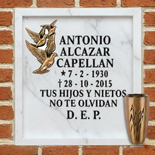 Lápida de columbario en mármol con palomas y jarrón de bronce, con inscripción conmemorativa en Madrid